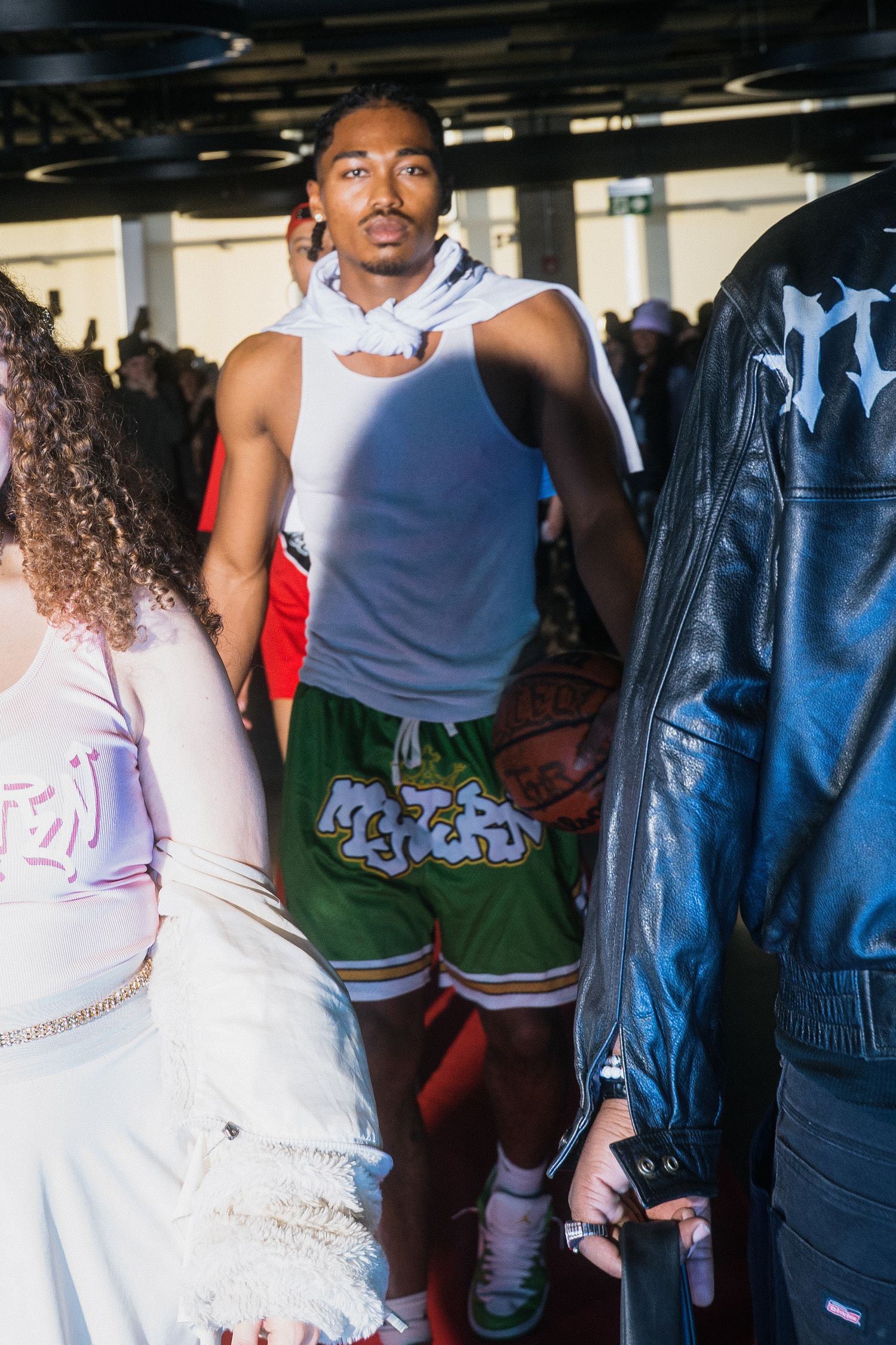 Male model poses in white cut tank top and green graffiti basketball shorts holding a basketball.