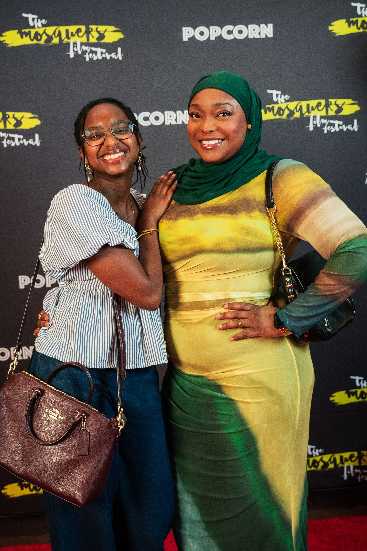 Two women smiling and posing together on a red carpet at the Mosque Film Festival event.