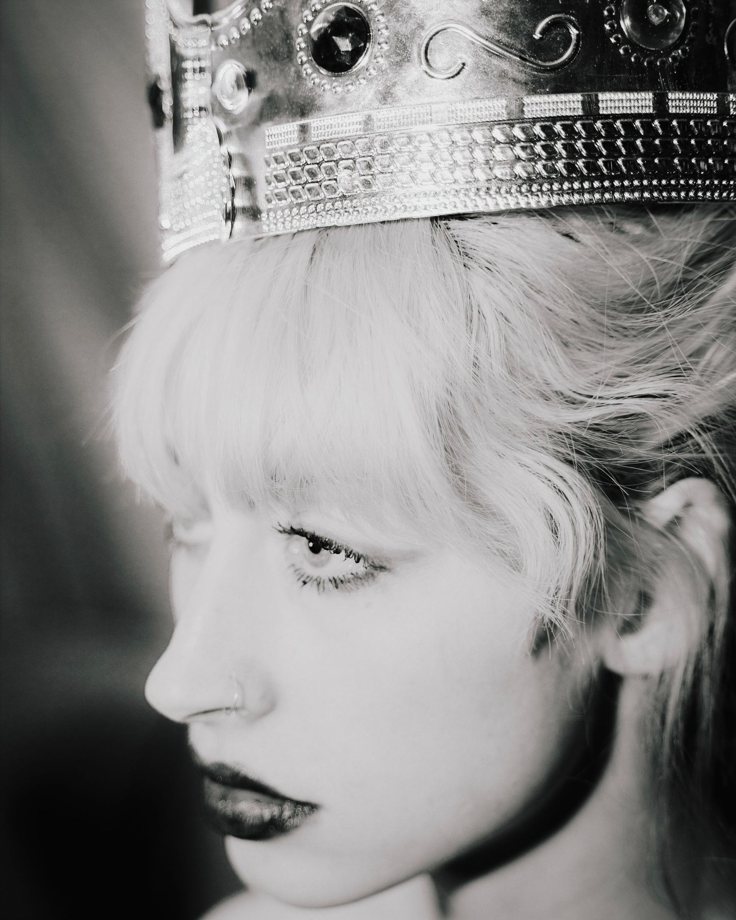 Black and white portrait of a blonde woman wearing an ornate jeweled crown, looking downward.