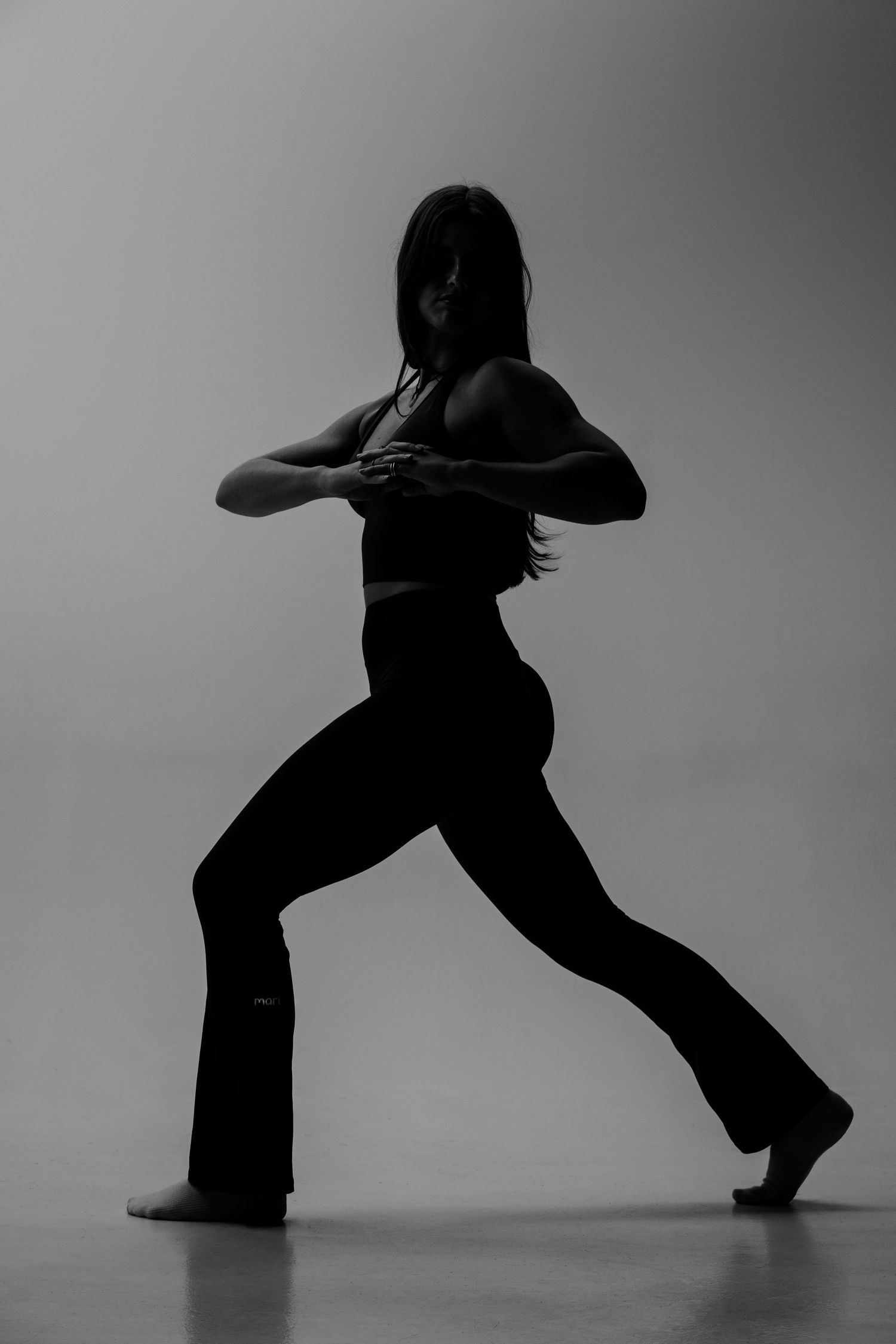 Silhouette of a woman dancing in flared pants and crop top against a grey background.
