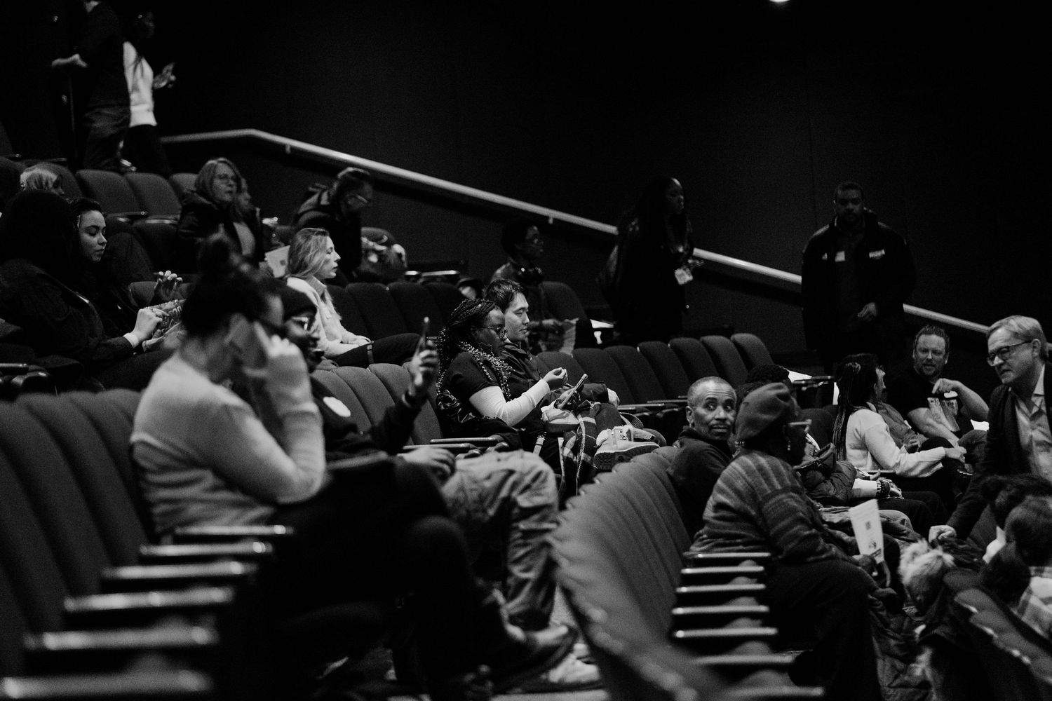 Diverse audience seated in dark theater during cultural event performance.