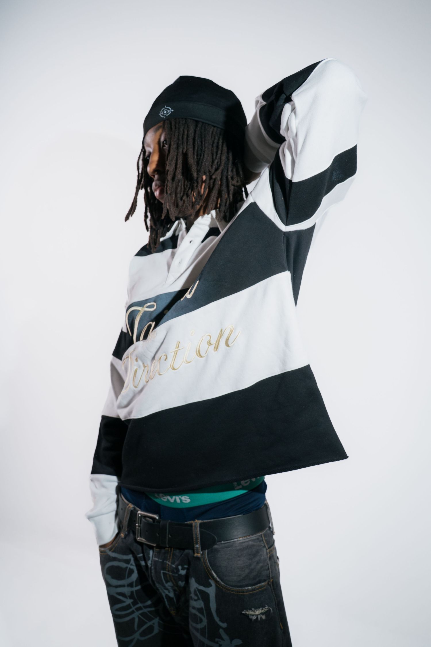Model in black and white striped rugby shirt with gold script, showing back view against white background.