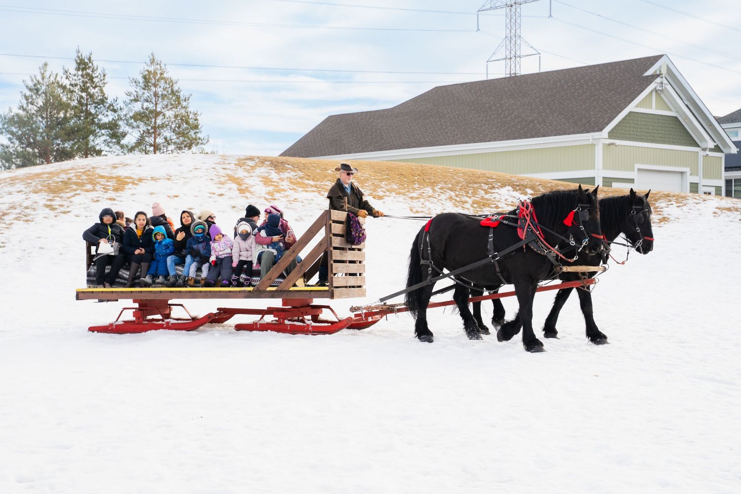 Two black horses pulling a red sleigh filled with children and adults through snowy winter landscape.