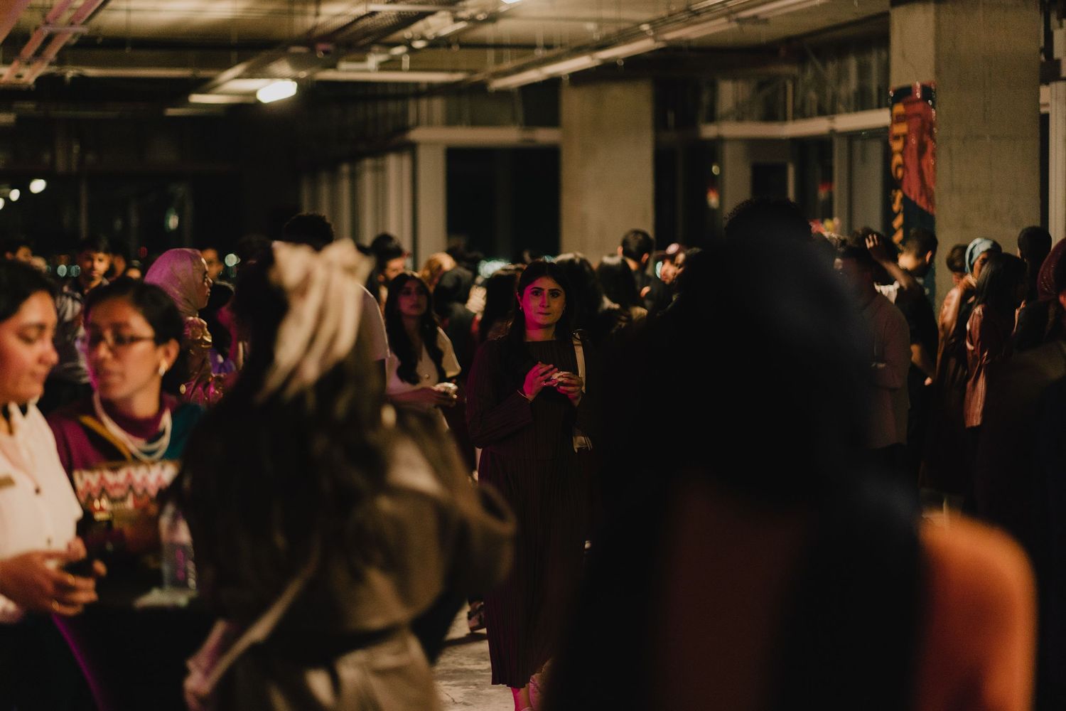 Crowd of people mingling in a dimly lit venue during an evening event or party.