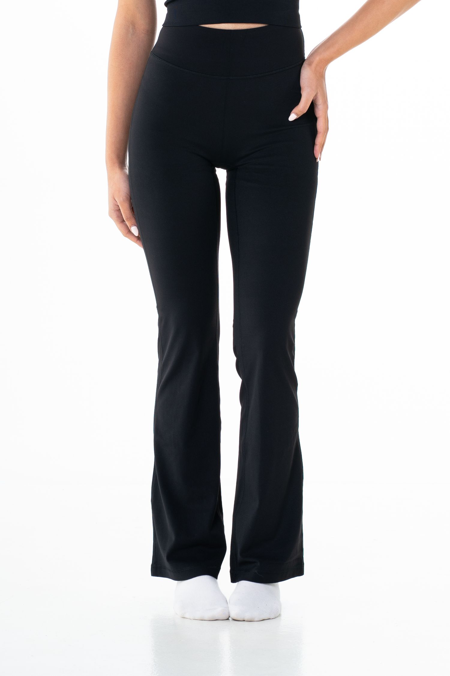 Woman wearing high-waist black flared leggings with a black crop top and white socks.