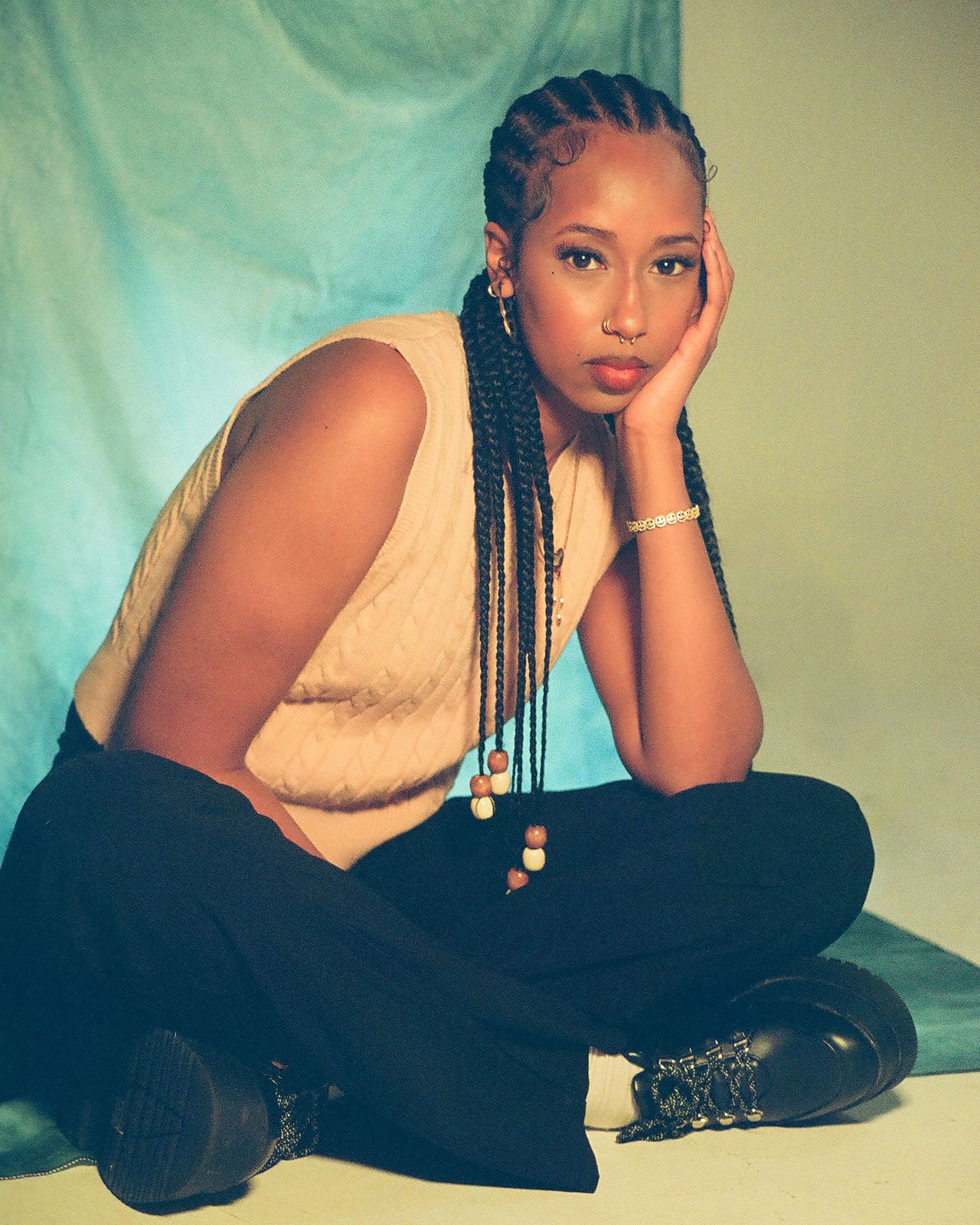 Young woman with box braids in beige top and black pants seated on floor.
