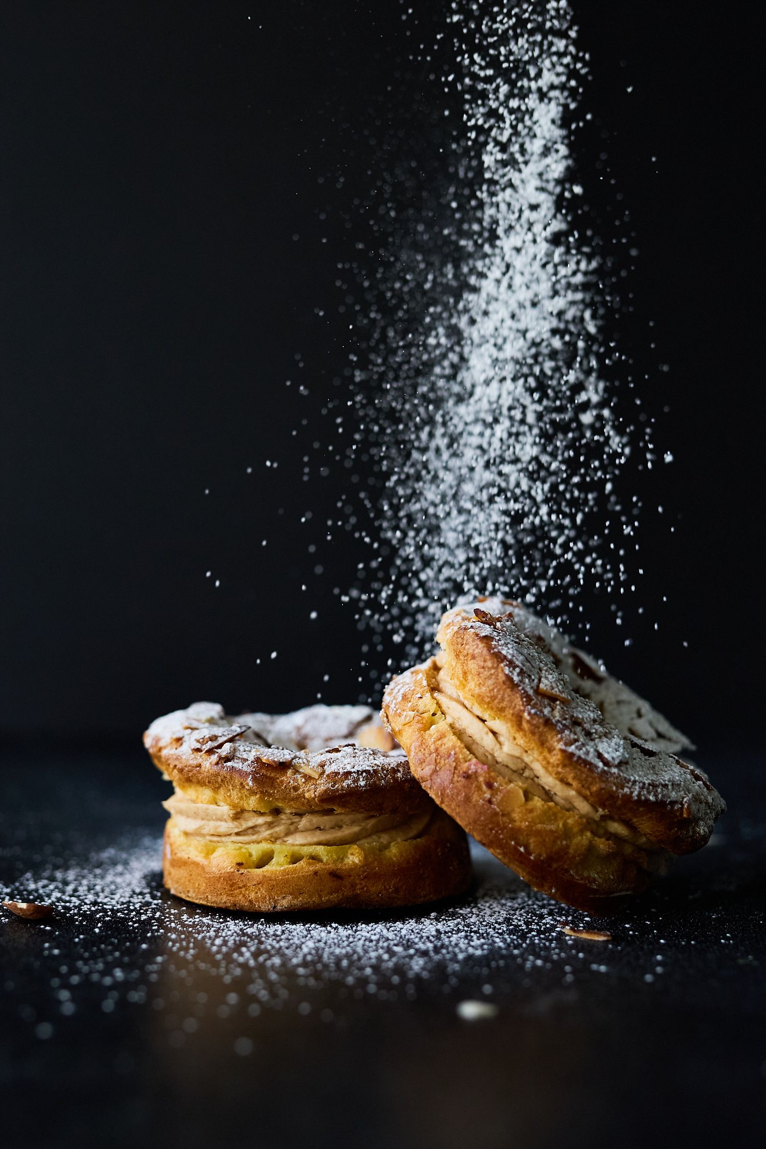 Golden pastries dusted with powdered sugar against a dramatic dark background.