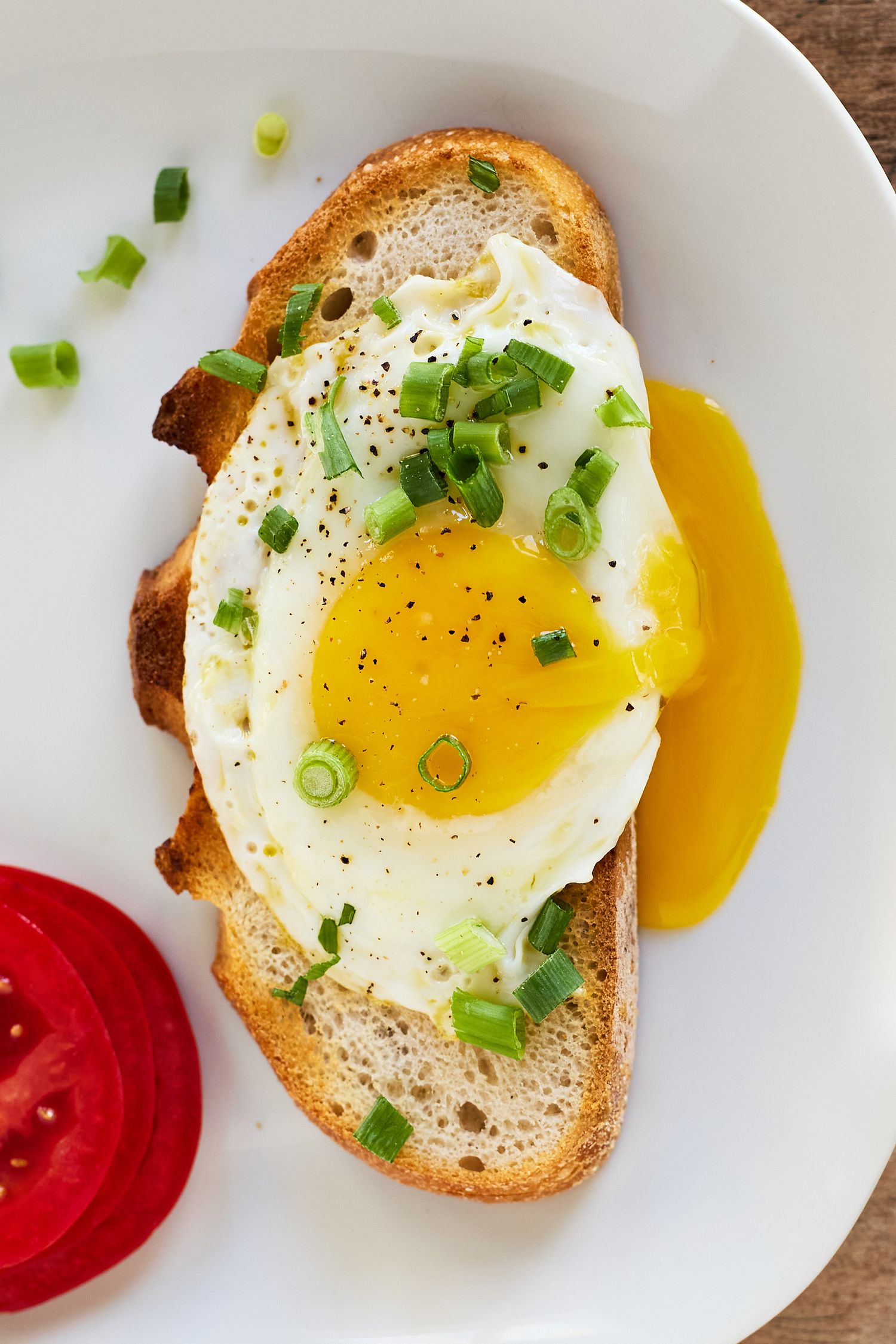 Overhead photograph of a fried egg on toasted bread garnished with herbs, accompanied by fresh tomatoes.