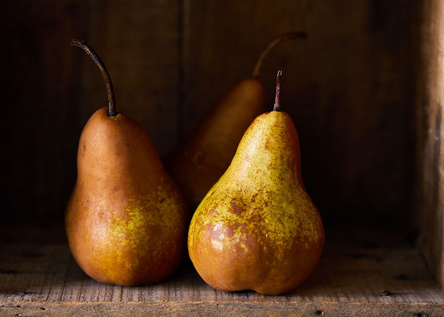 Two ripe pears illuminated by soft, directional light against a dark, rustic background.