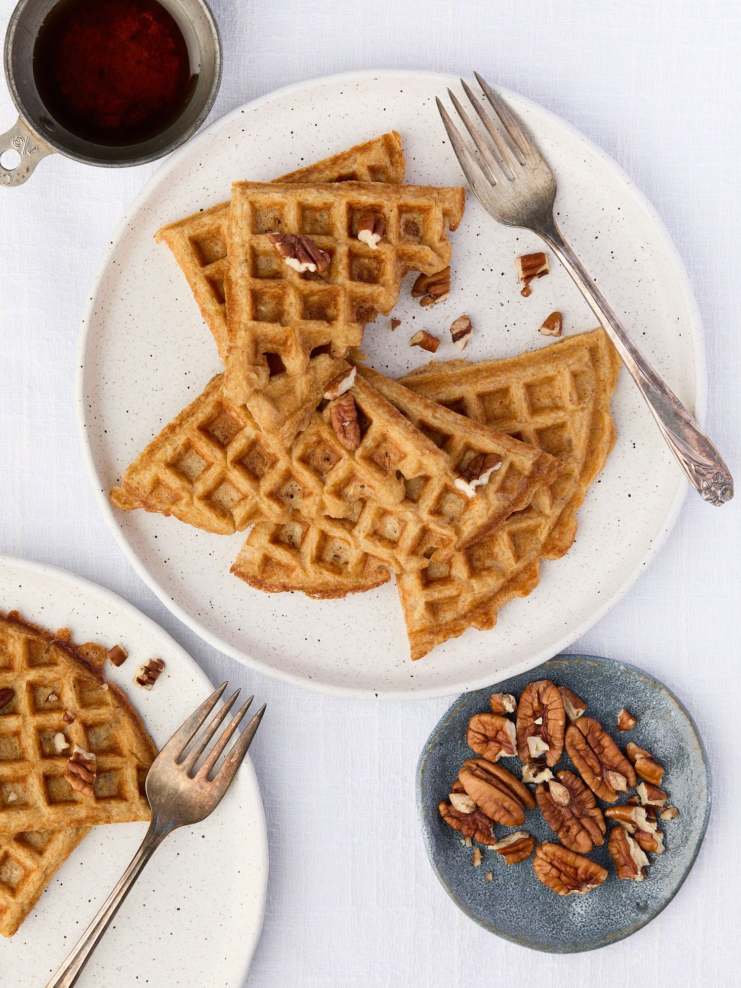 Overhead food photograph of GoodGate Foods waffles on white plates with forks, a bowl of almonds, and maple syrup on a light background.