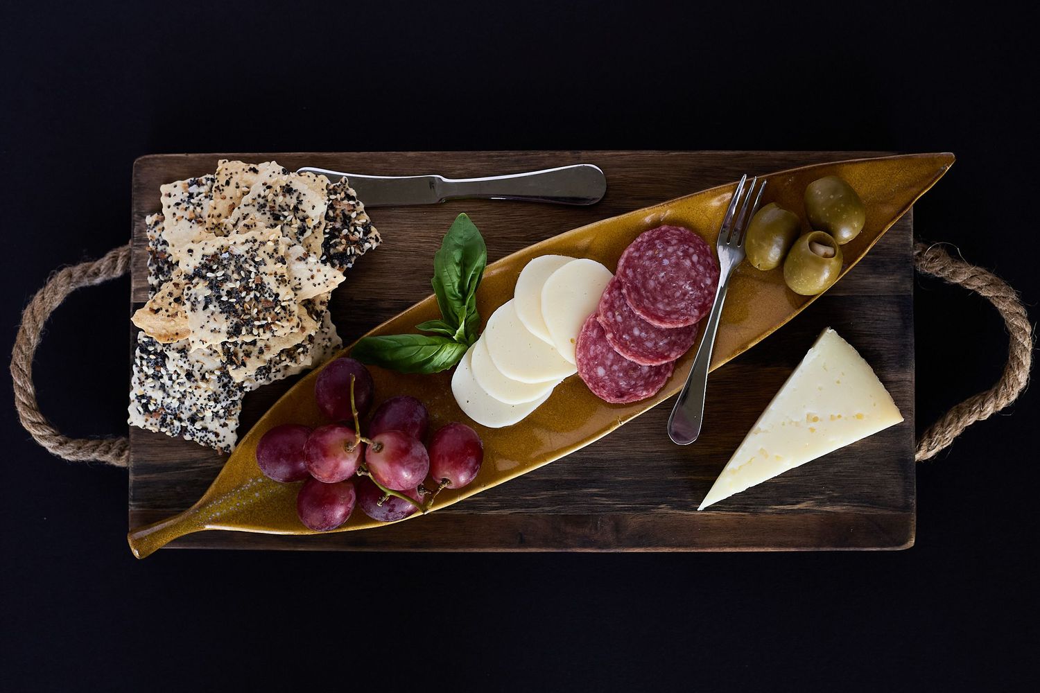 Overhead charcuterie board with artisan cheeses, salami, crackers, grapes, and olives arranged on a wooden serving tray.