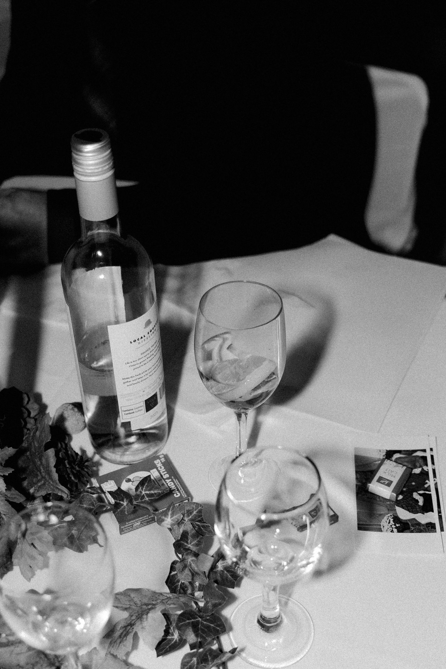 Black and white photo of wine bottle and glasses on a decorated wedding reception table.