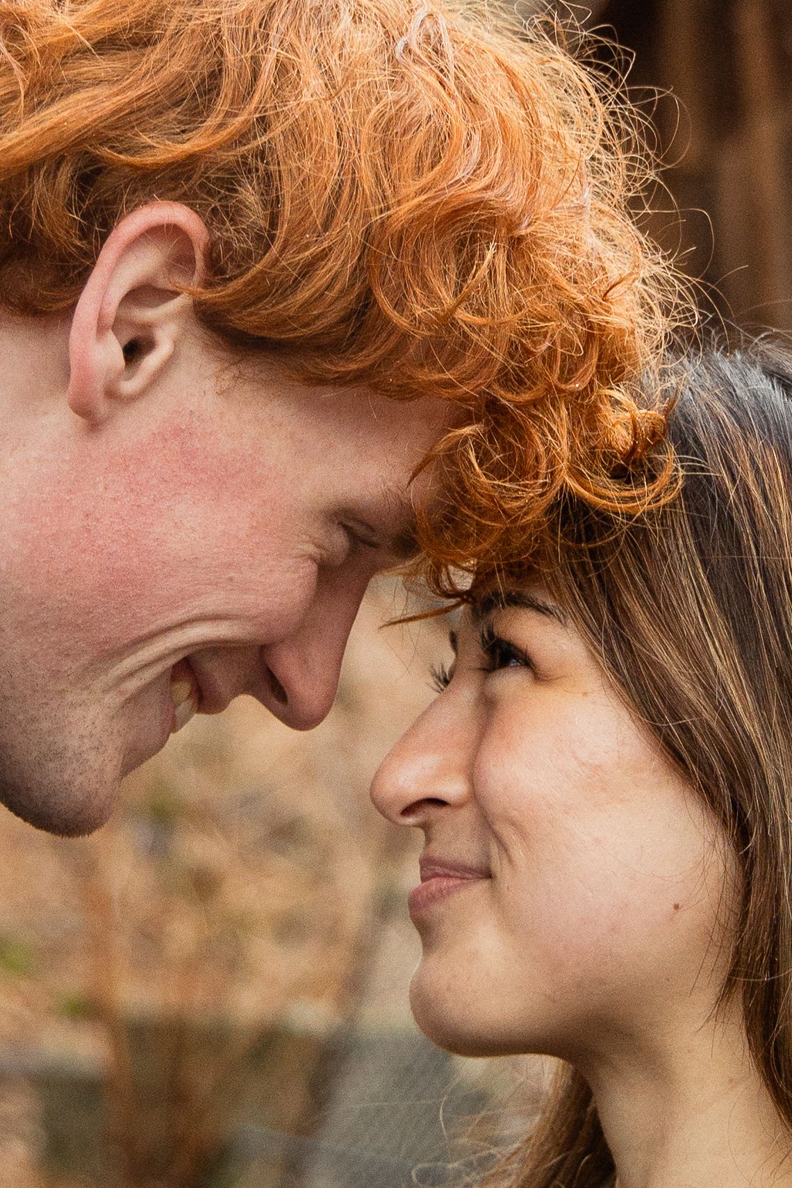 Close-up of a smiling couple touching foreheads romantically, man with curly red hair outdoors.
