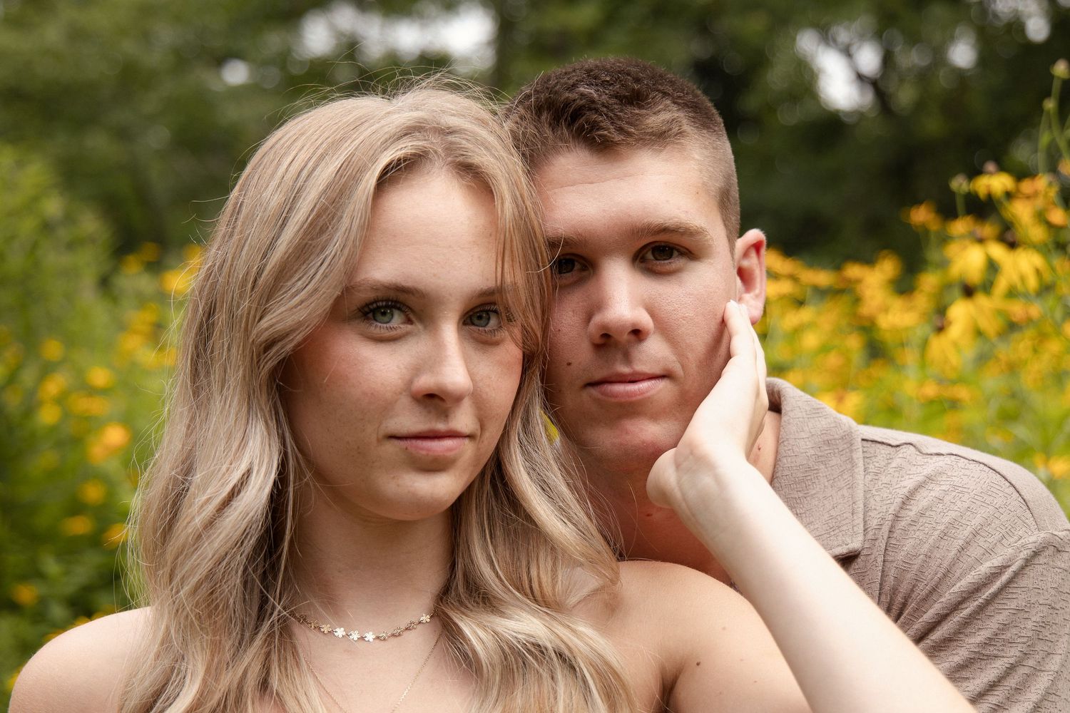 Young couple posing together in front of yellow wildflowers in a lush green garden.