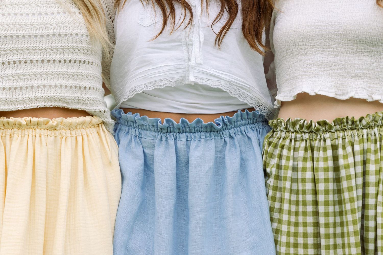 Close-up of three women wearing white crop tops and pastel midi skirts in yellow, blue, and green gingham.