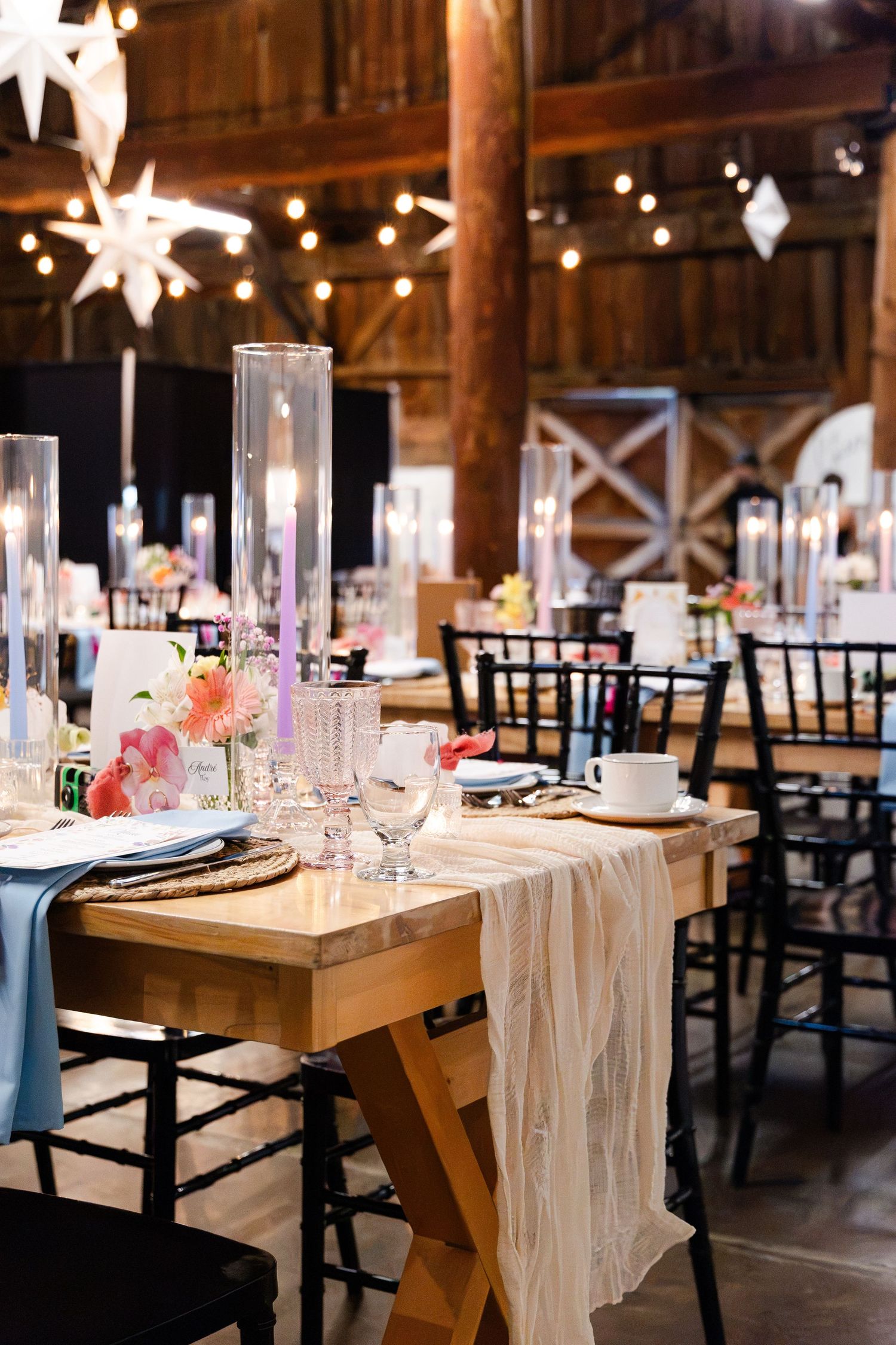 Elegant barn wedding reception with string lights, tall candles, and floral centerpieces on wooden tables.