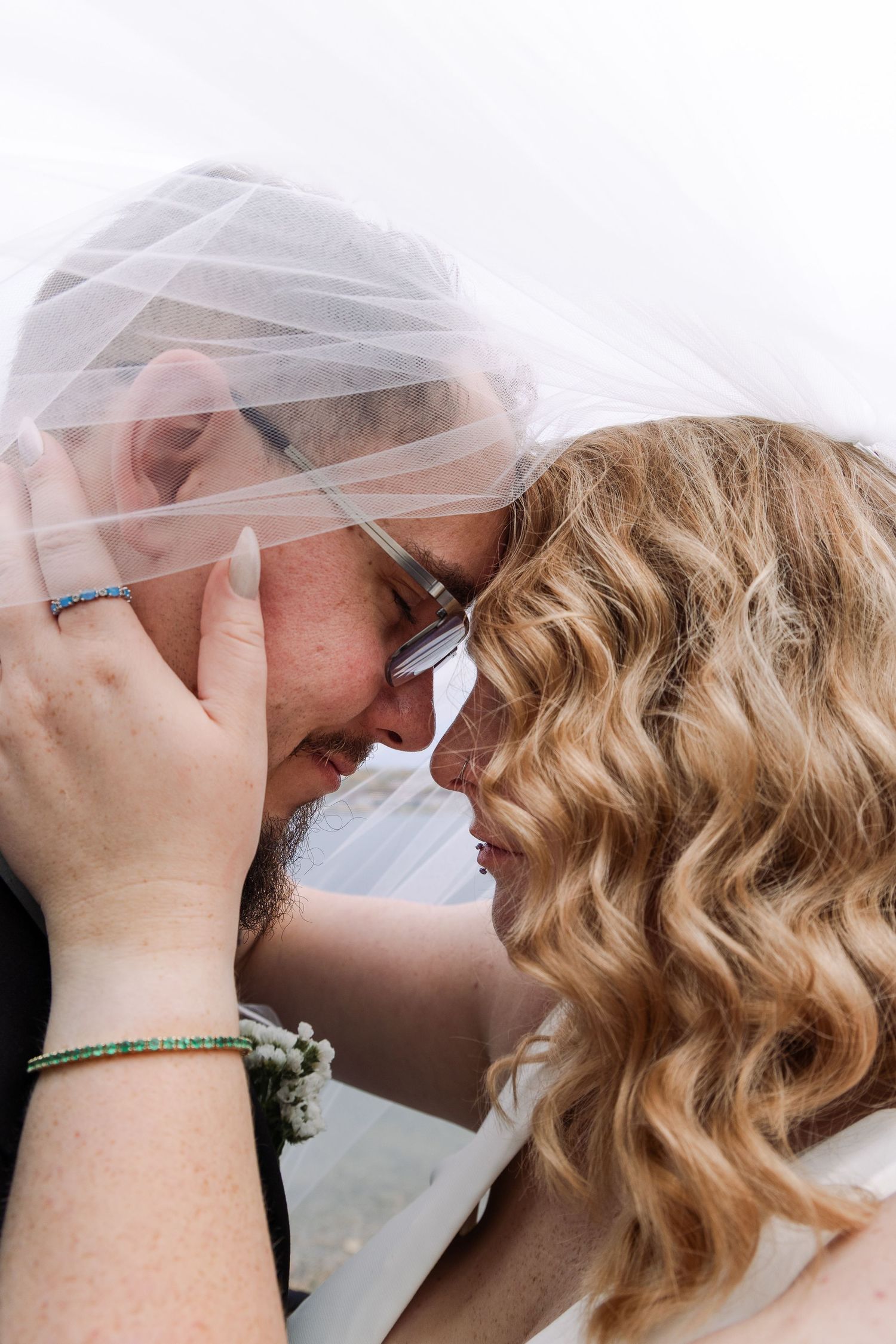 Bride and groom sharing a tender forehead-to-forehead moment under a flowing white wedding veil.