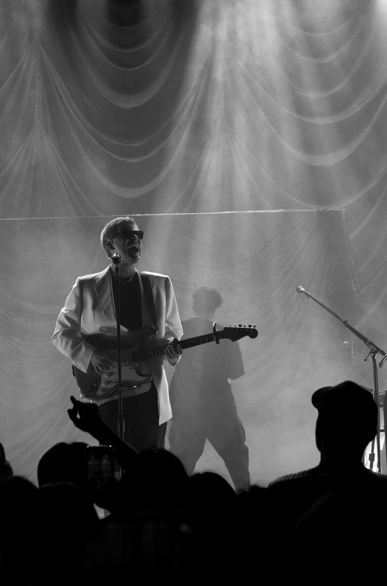 Black and white concert photo of guitarist in white blazer performing on stage with dramatic lighting.