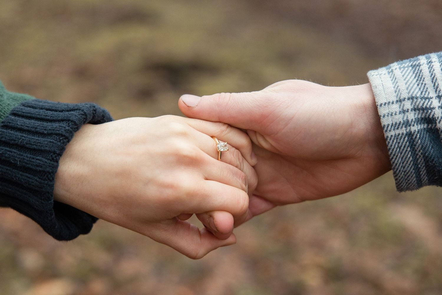 Close-up of couple holding hands showing an engagement ring, wearing knit and plaid sleeves.