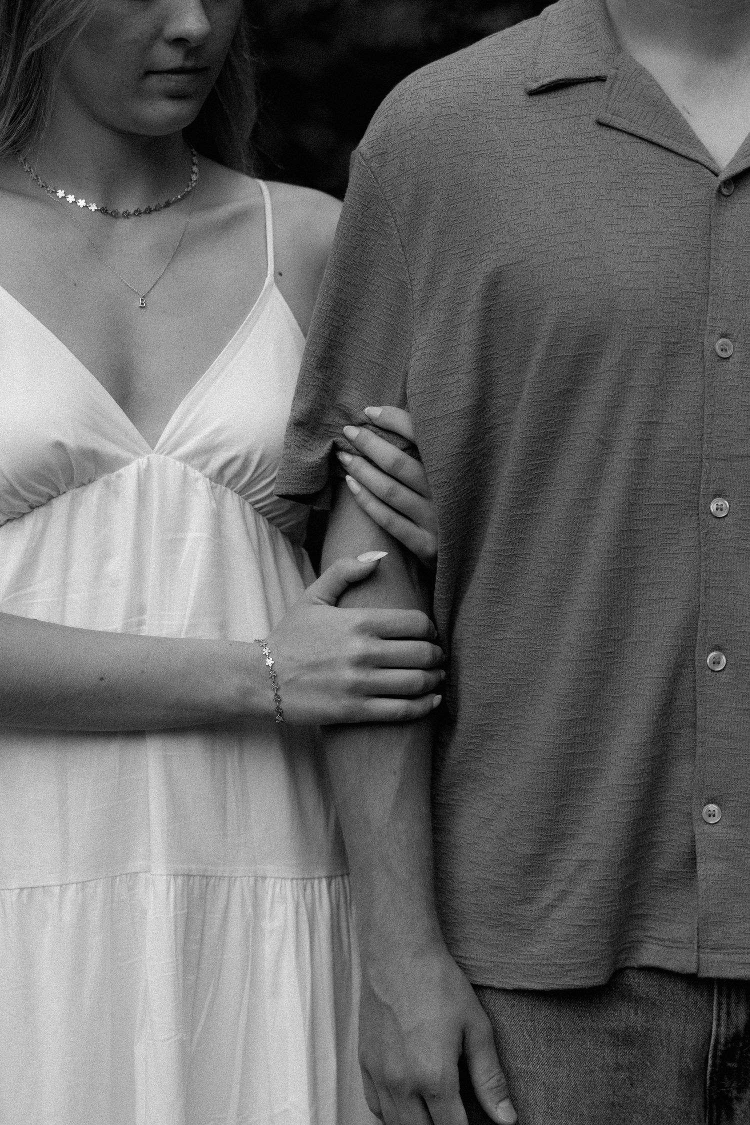 Black and white close-up of woman in white dress holding mans arm in intimate engagement photo.
