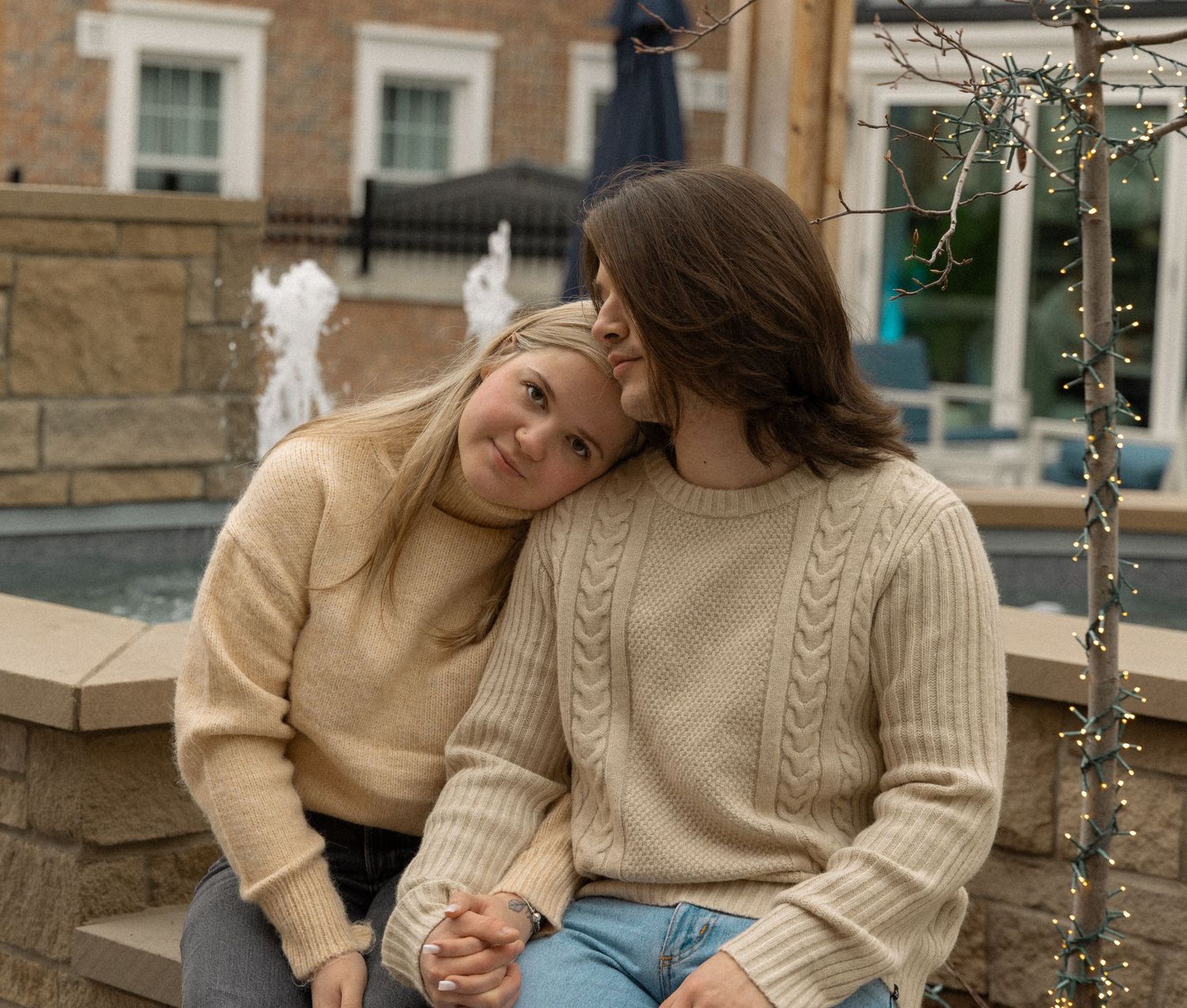 Young couple in matching cream cable-knit sweaters sitting together as man kisses woman on forehead.