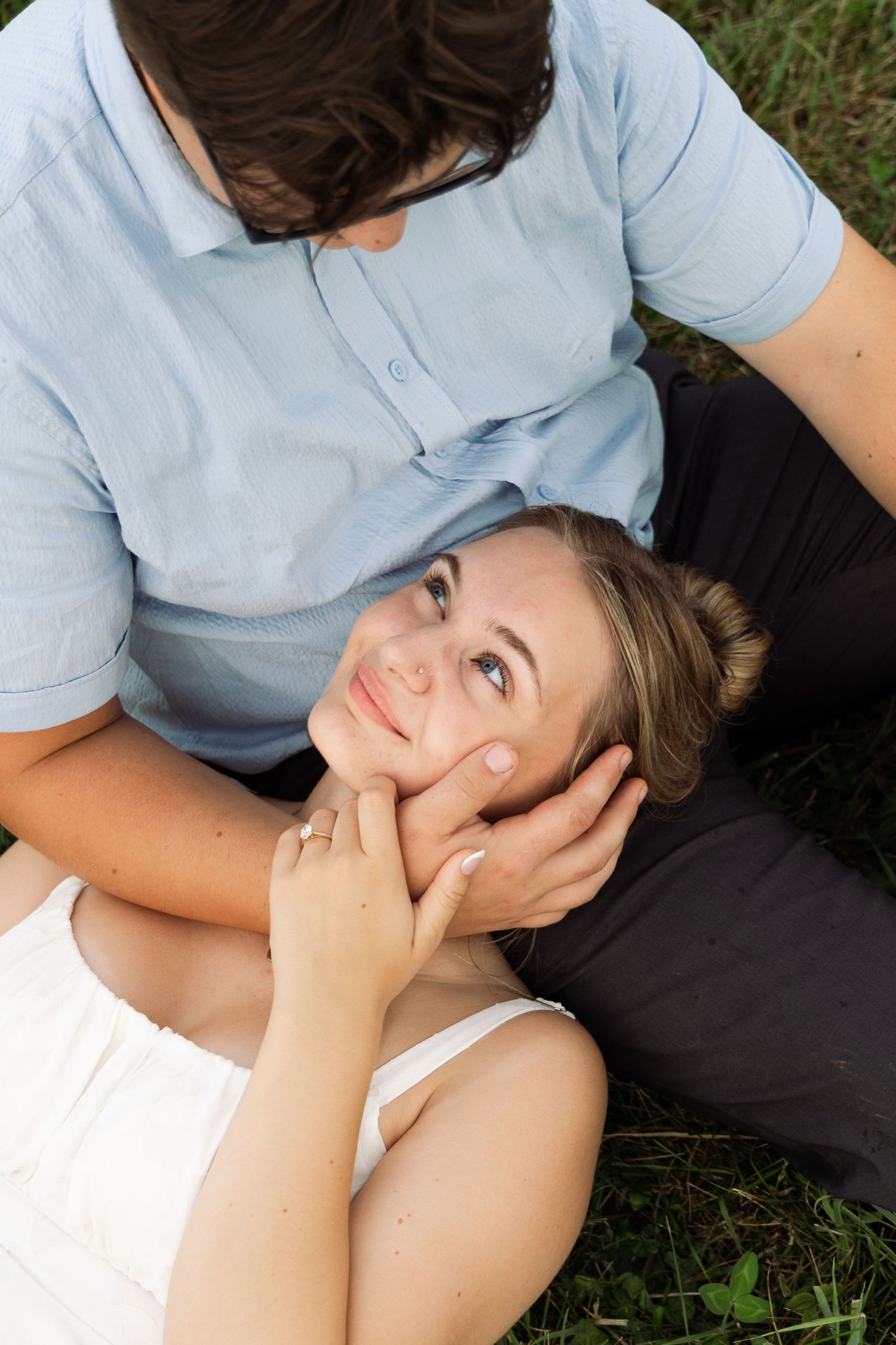 Woman lying on grass looking up at man who gently cradles her face in his hands.