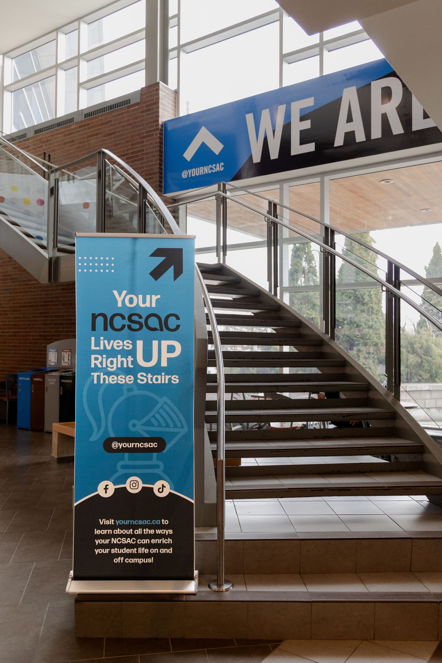 NCSAC student organization banner beside staircase with WE ARE sign in university building.
