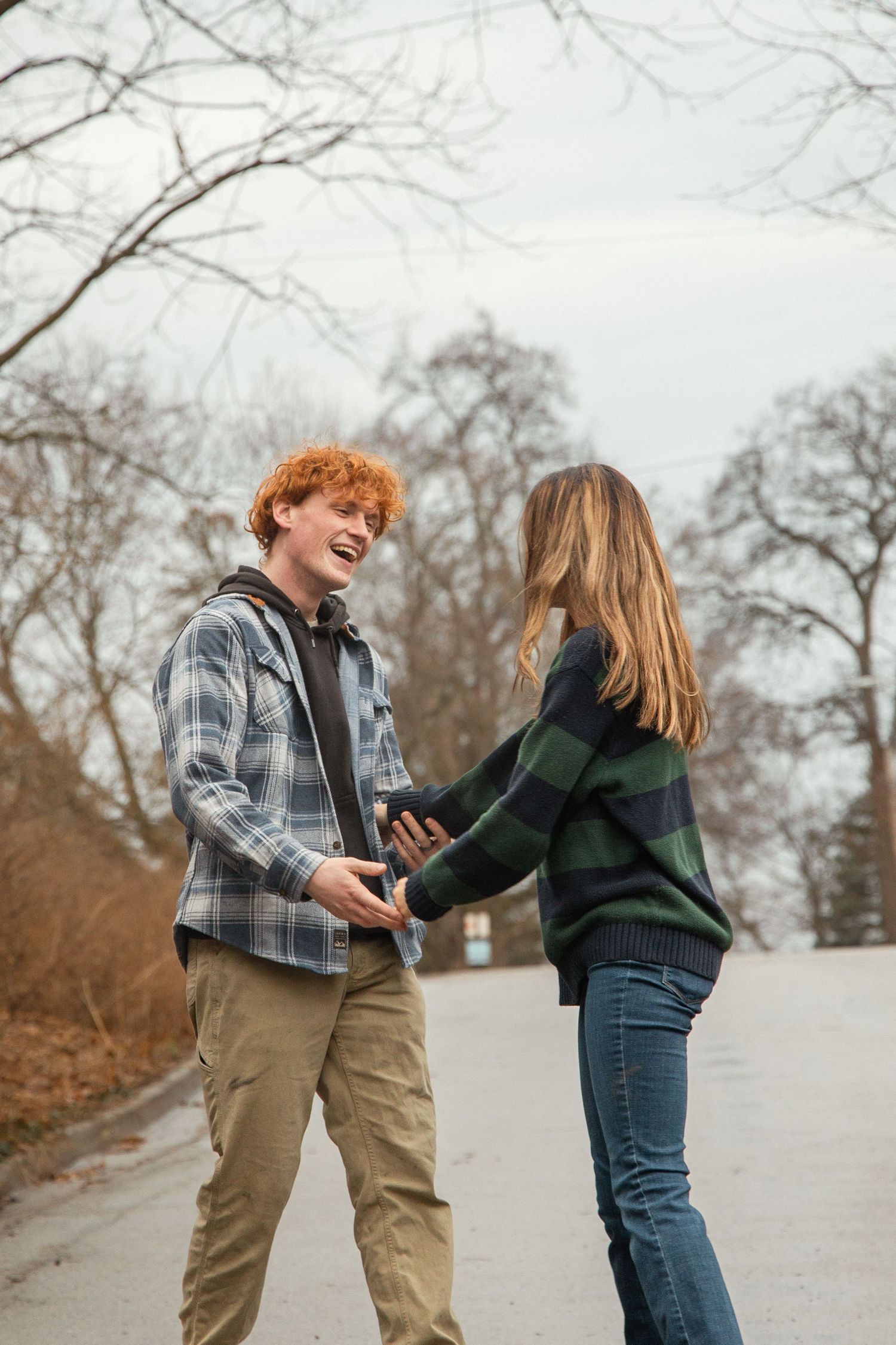 Happy redhead man laughing with girlfriend holding hands on a tree-lined path in autumn.