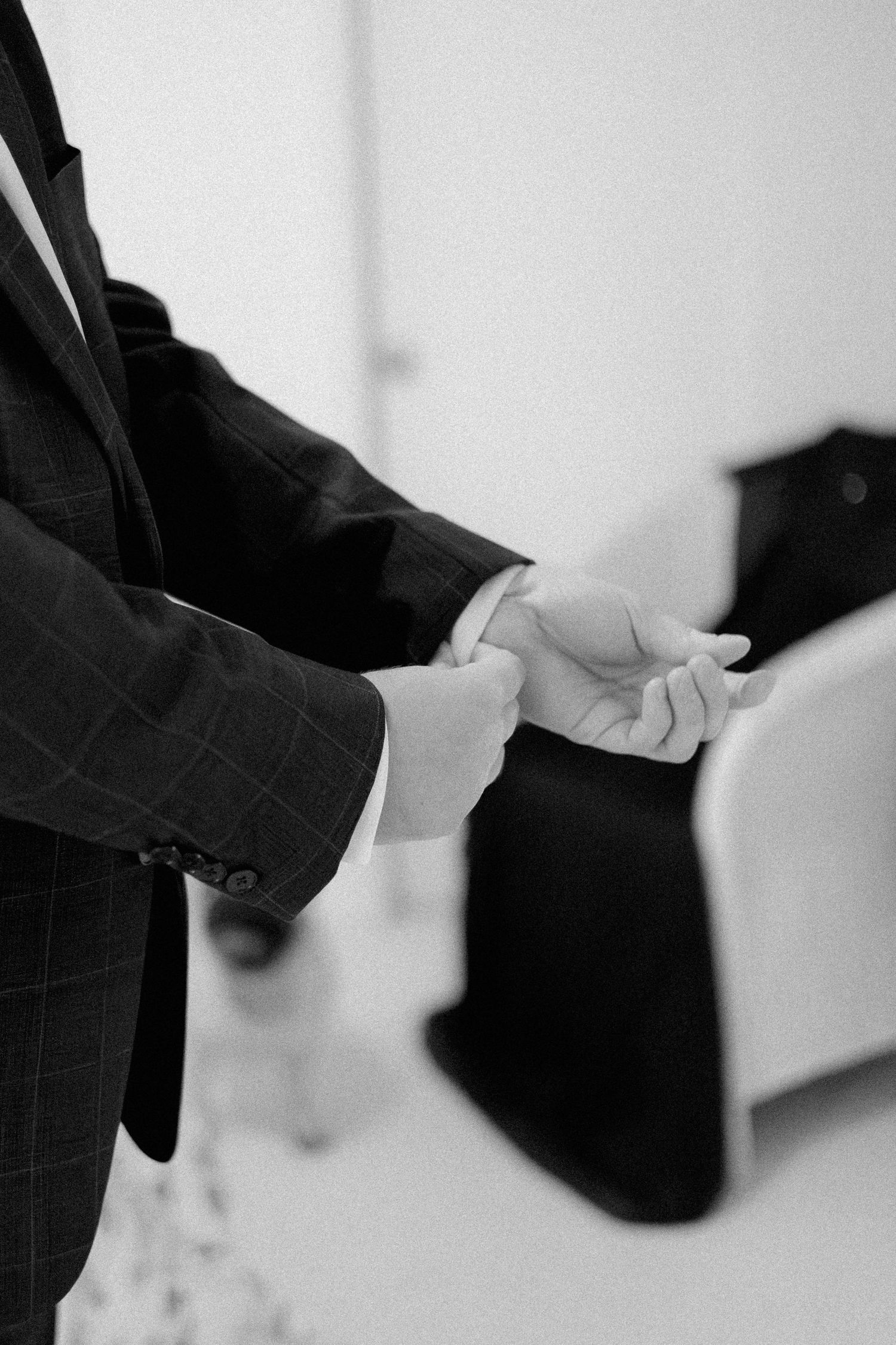Black and white photo of groom in plaid suit adjusting his cufflinks before wedding ceremony.