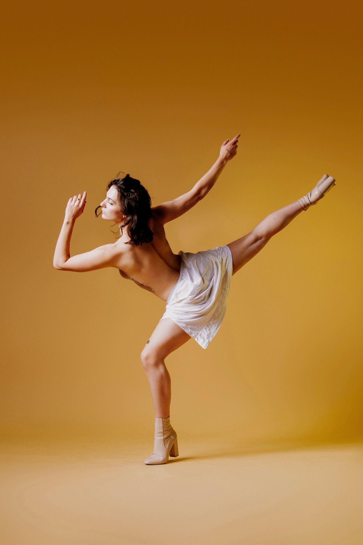 Contemporary dancer in white performs graceful arabesque sequence against warm golden backdrop.