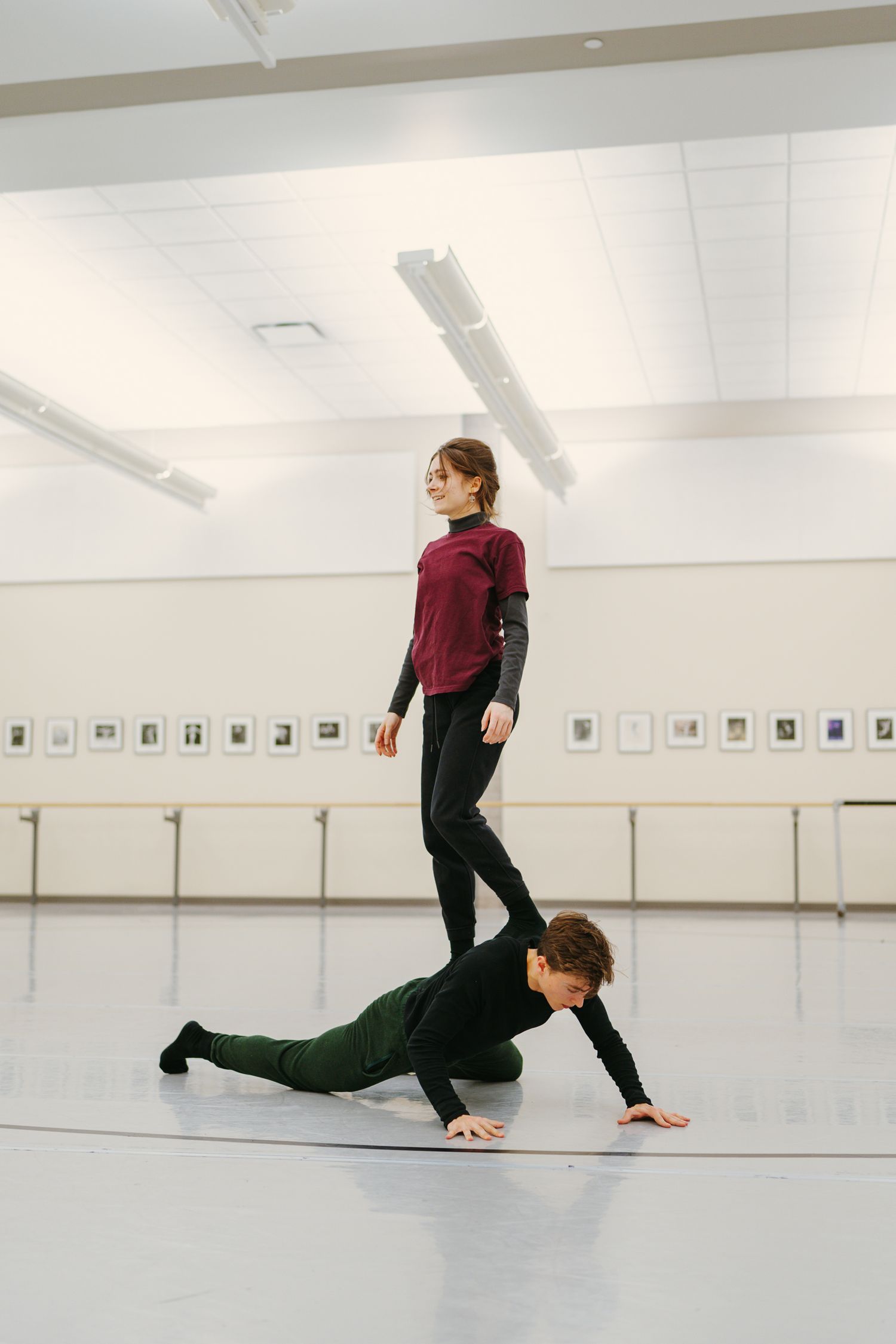 A dancer in burgundy top and dark pants performs a graceful floor sequence in a bright studio space.