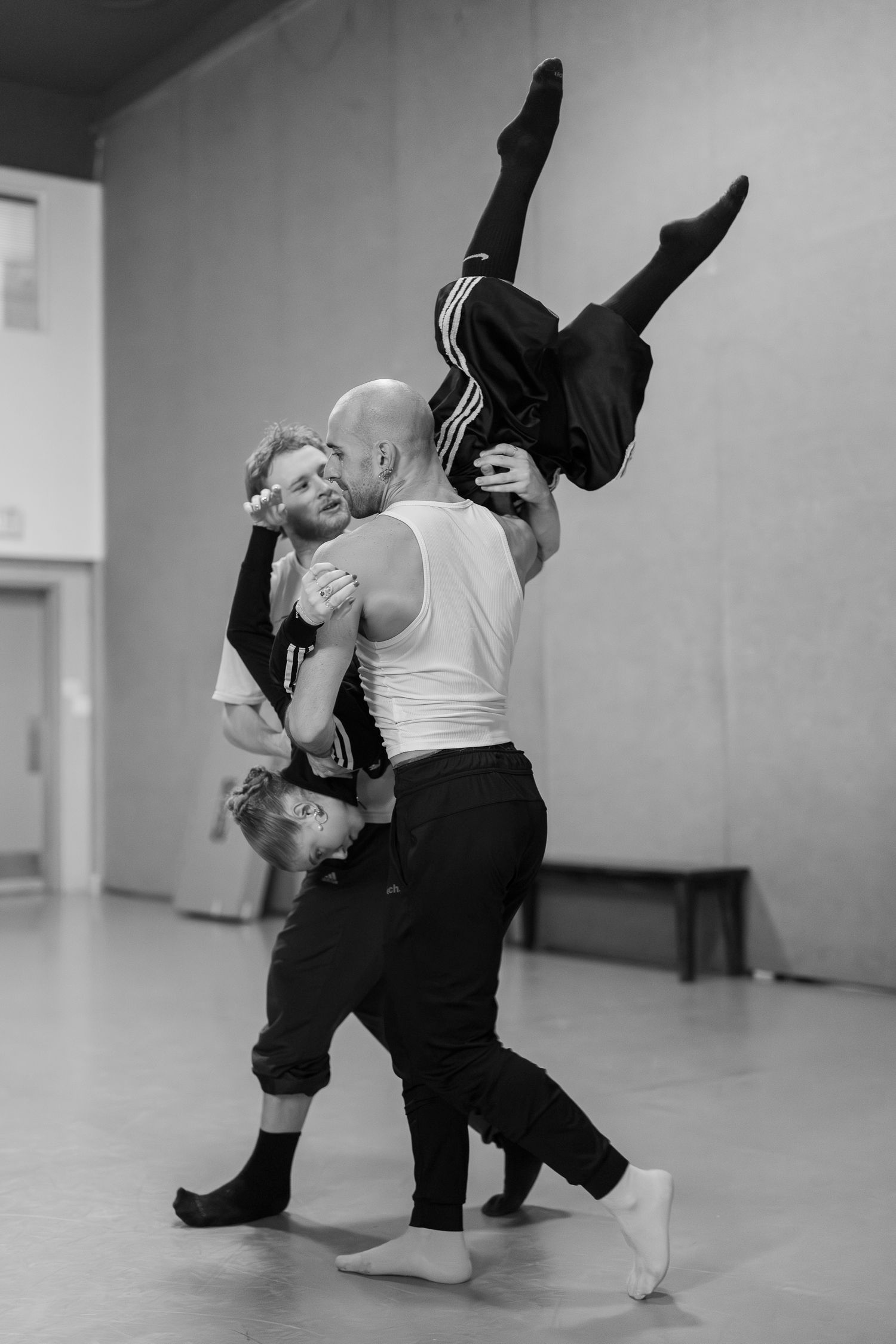 Two dancers perform a contemporary dance routine in a minimalist studio space, captured in black and white.