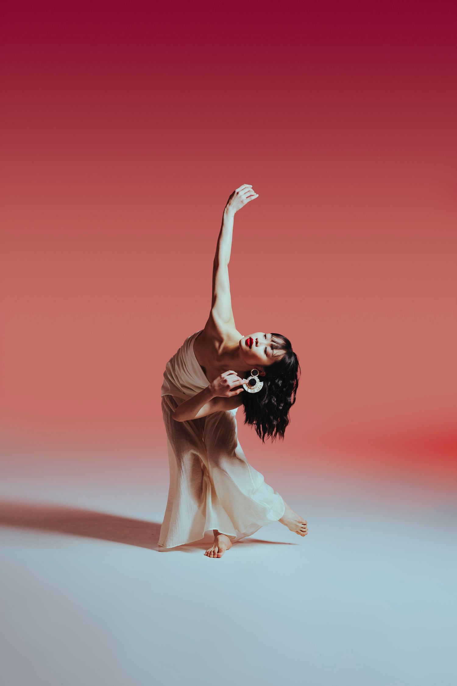 A dancer in flowing fabric performs an elegant backbend against a red gradient background.