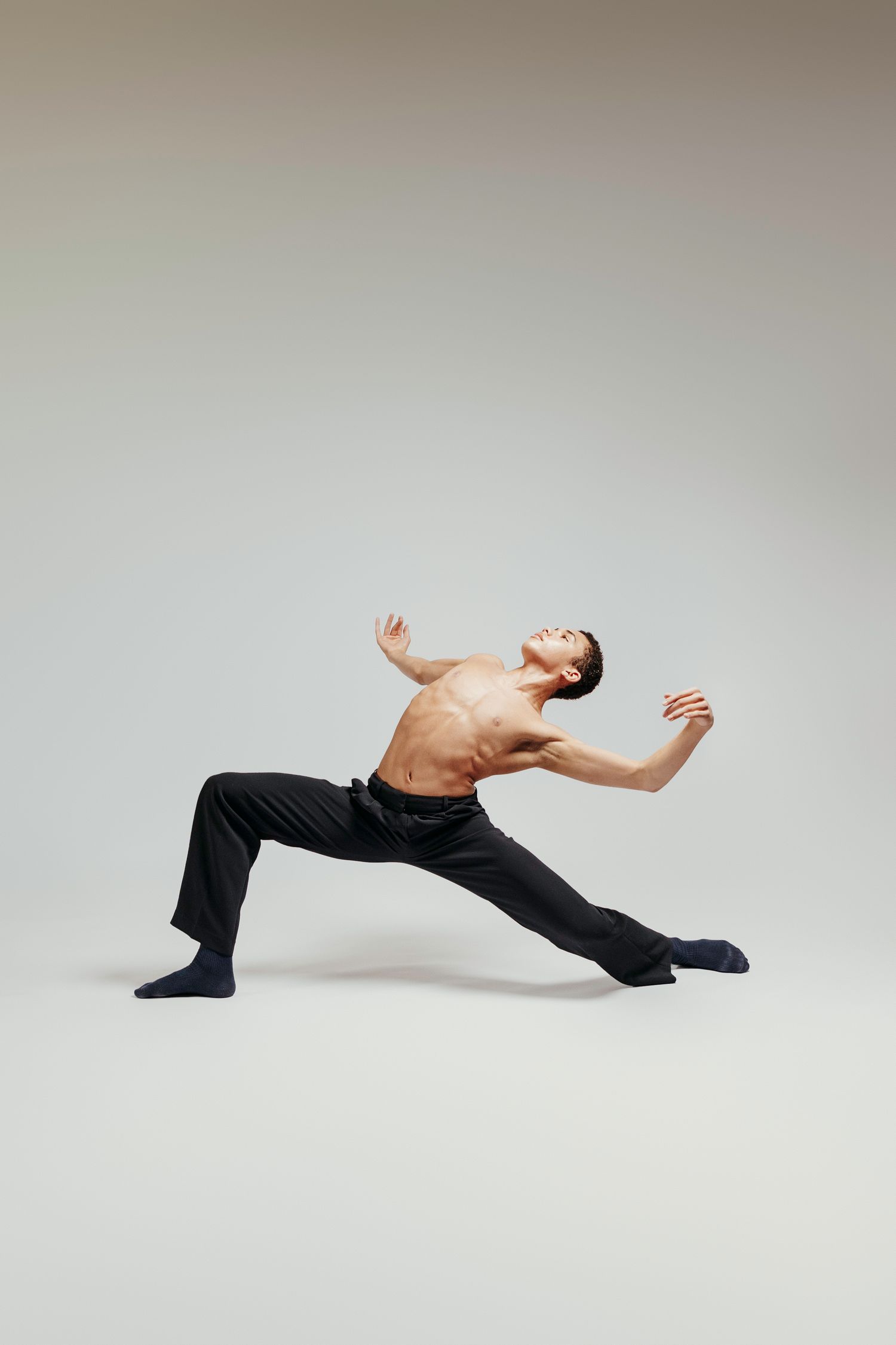 A dancer performs a graceful contemporary dance sequence in black pants against a white studio backdrop.