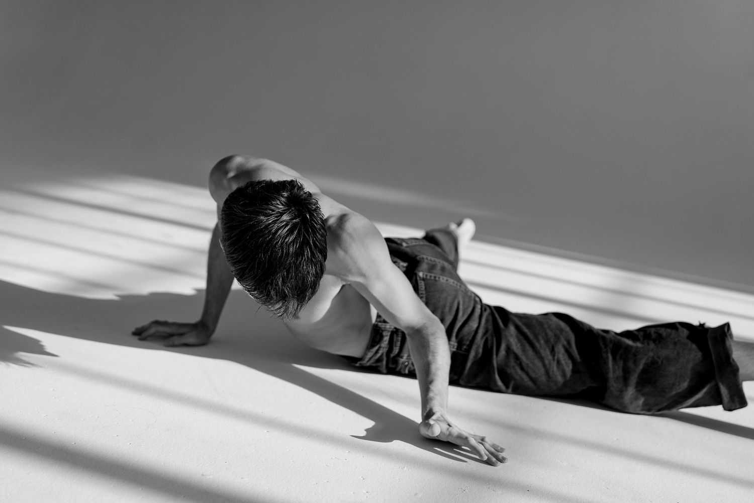 Person lying on floor in dramatic lighting doing push up exercise in black and white photography.