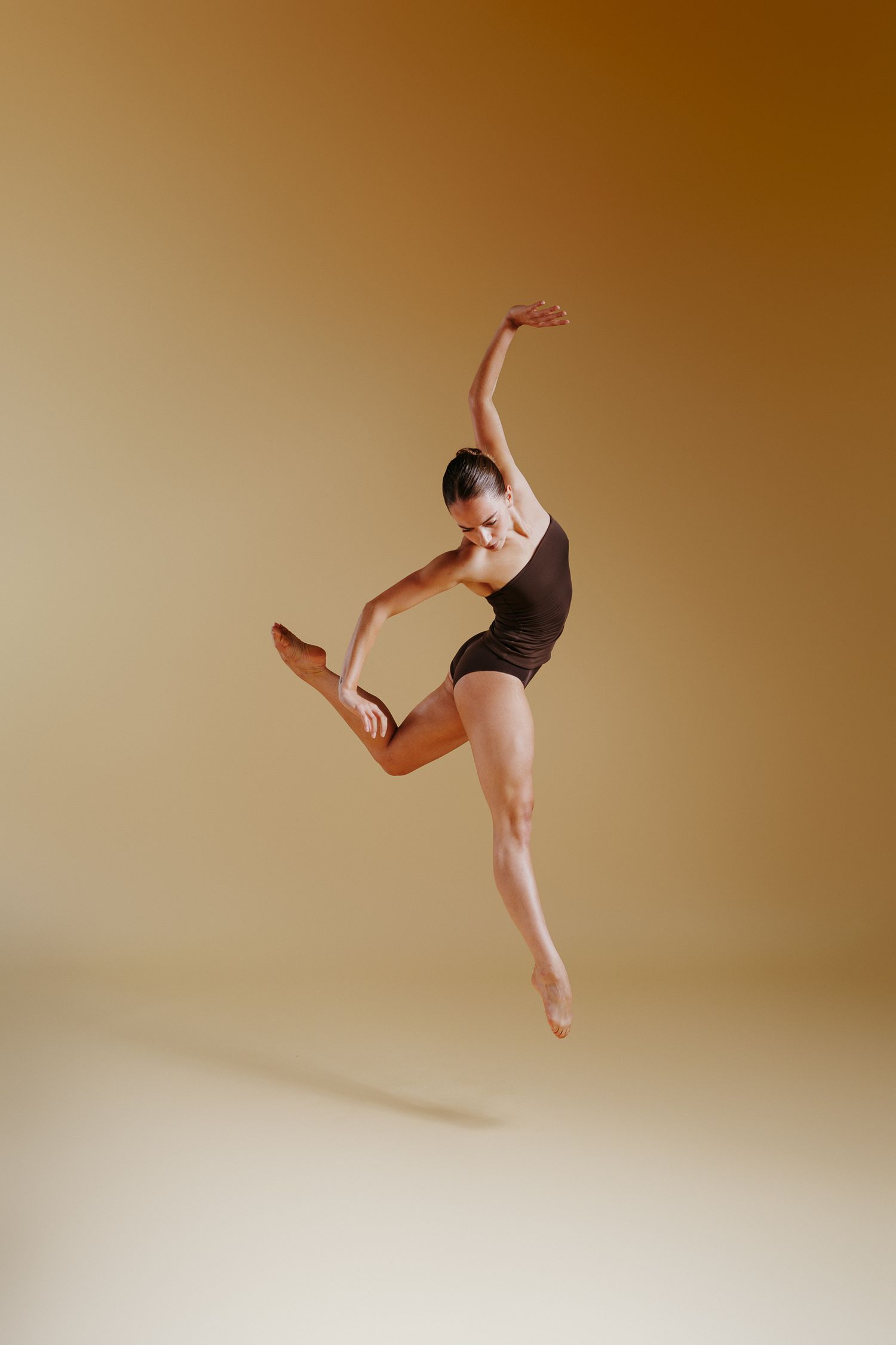 A graceful dancer performs a dynamic leaping sequence across a studio space with warm brown lighting.