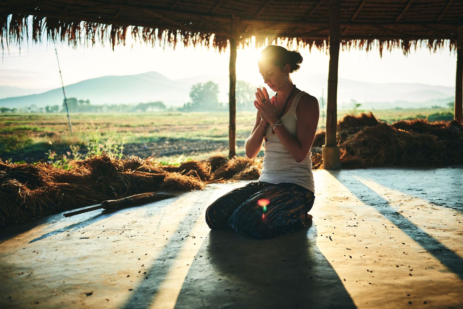 Woman meditating in lotus pose at sunrise in an open-air pavilion with scenic mountain and field views.
Lotus Land.Photo