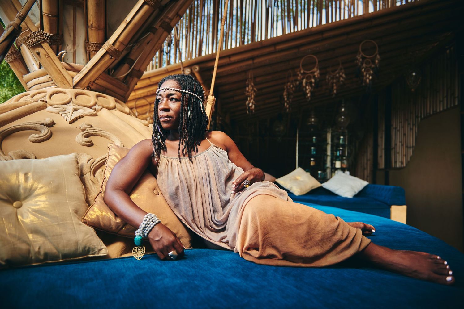 A woman with braided hair reclines gracefully on a blue velvet surface in a bohemian-styled room.
Lotus Land.Photo