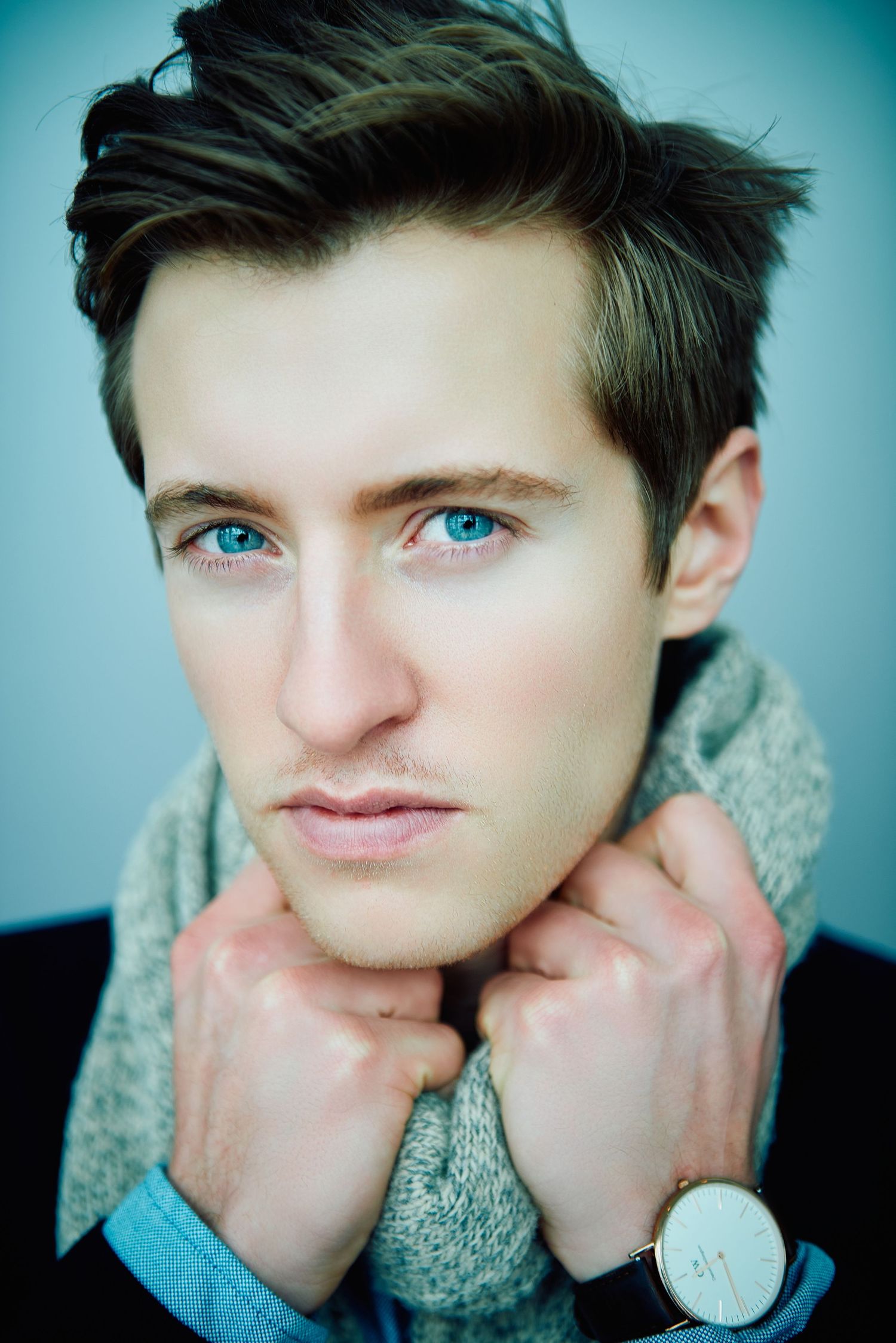 Young man with blue eyes and dark hair wearing a gray scarf and watch, posing for a close-up portrait photo.
Lotus Land.Photo