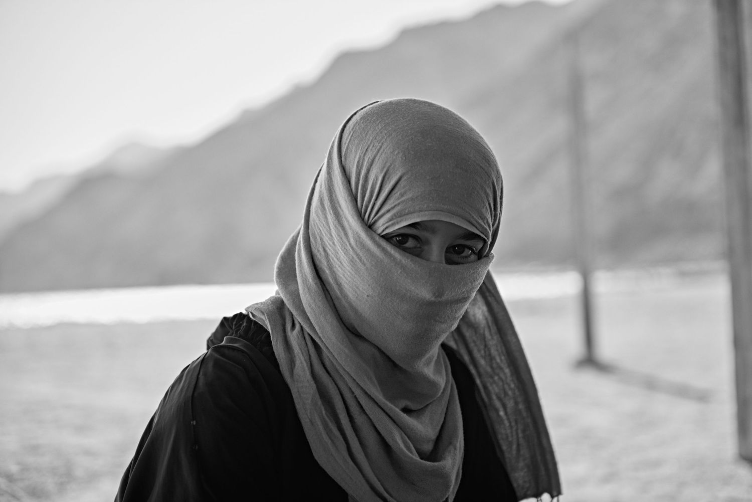 Black and white portrait of a woman wearing a hijab and niqab with mountains in the background.
