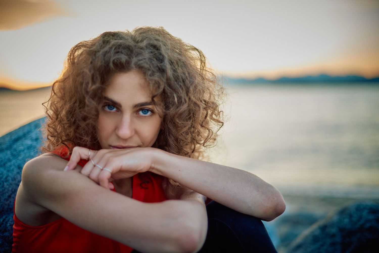 Curly-haired woman in red dress poses thoughtfully by a lake at sunset.
Carmel Amit
Lotus Land.Photo