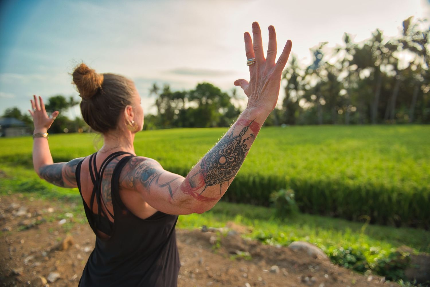 Tattooed woman in tank top practicing yoga outdoors near lush green rice fields at sunset.
Lotus Land.Photo
