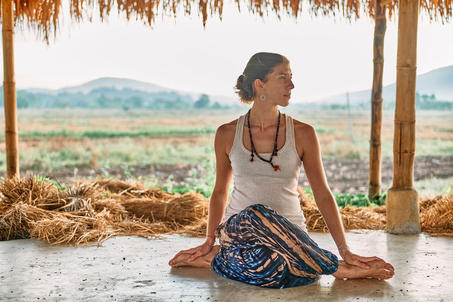 Woman practicing yoga in lotus pose under a rustic thatched shelter with scenic rice fields in background.
Lotus Land.Photo