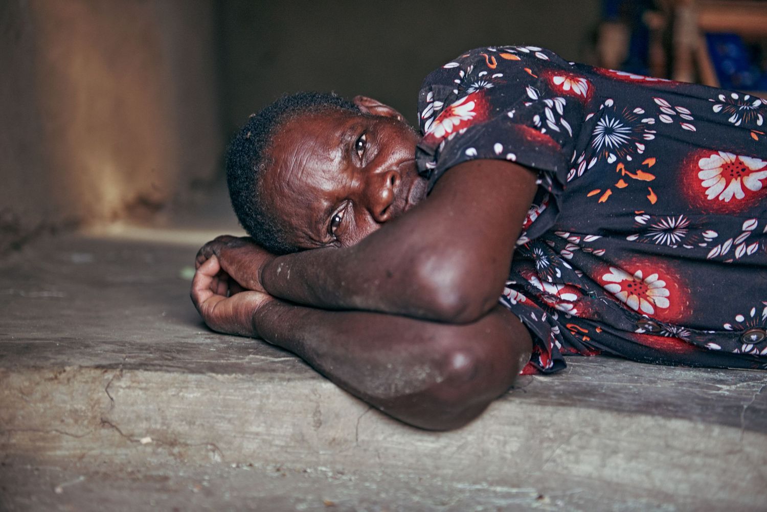A person in a floral dress lying on a wooden floor, resting their head on their arm.