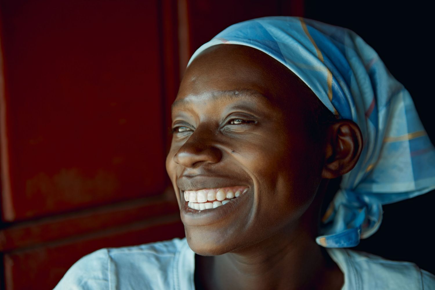 Joyful African woman wearing a light blue headscarf smiling brightly indoors.