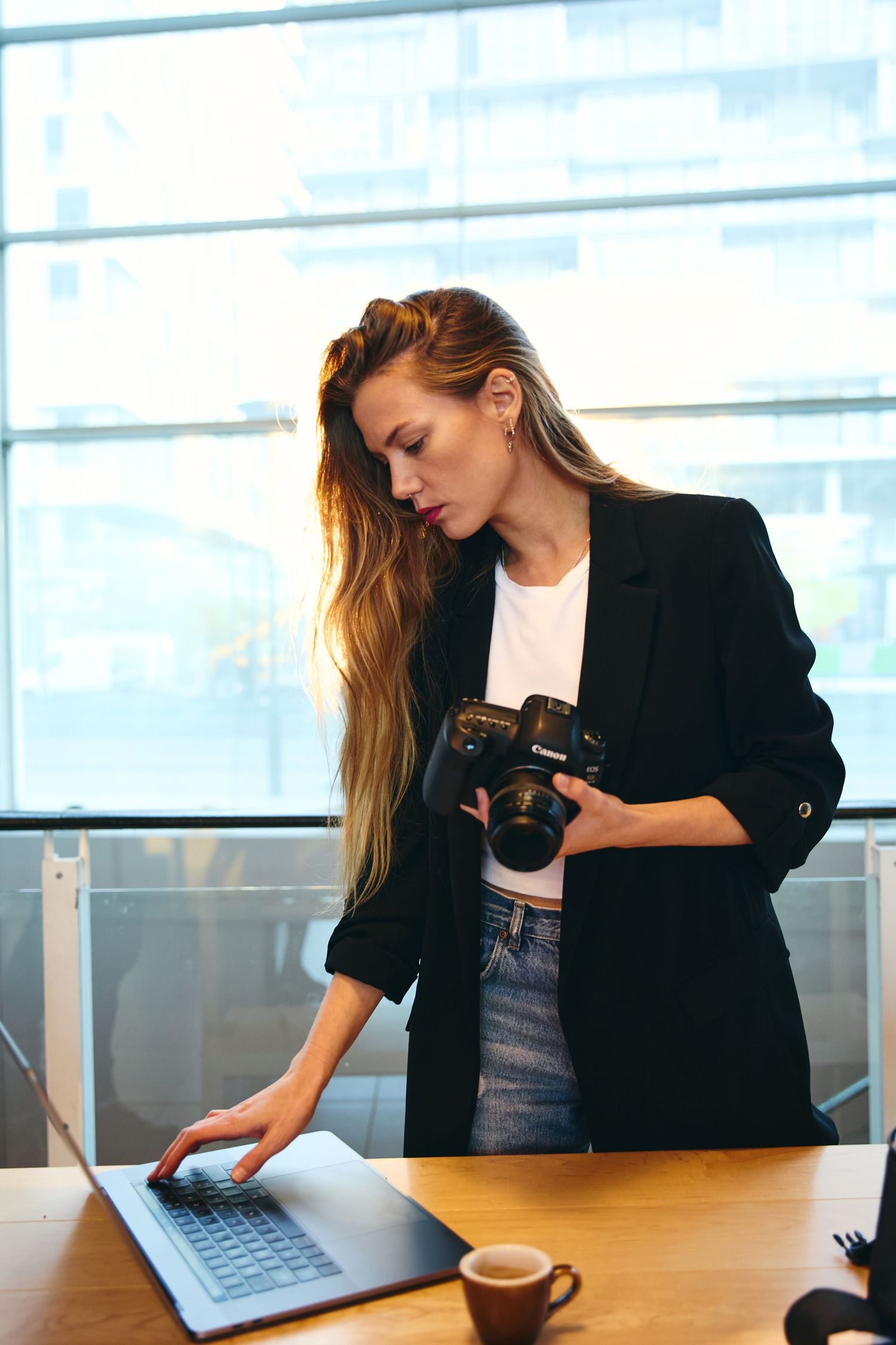 Female photographer holding a DSLR camera while working on a laptop in a modern office with large windows.
Lotus Land.Photo