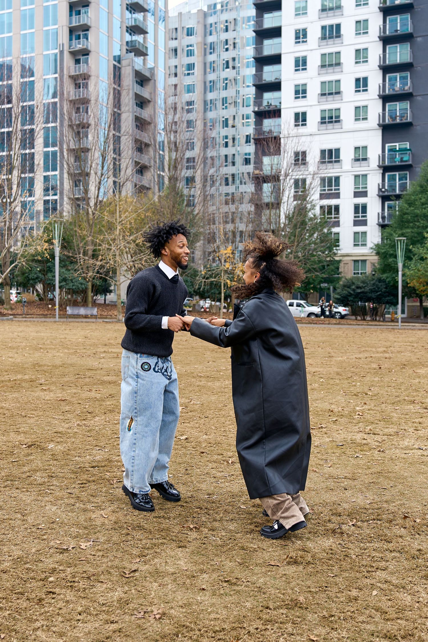 Two people share a lighthearted moment in an urban park with tall apartment buildings in the background. North Carolina Wedding Photographer