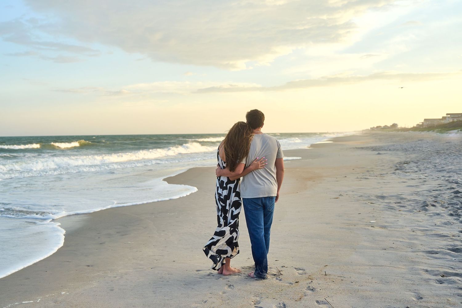 Two people walking together along a peaceful ocean beach at sunset while waves gently roll onto the shore.