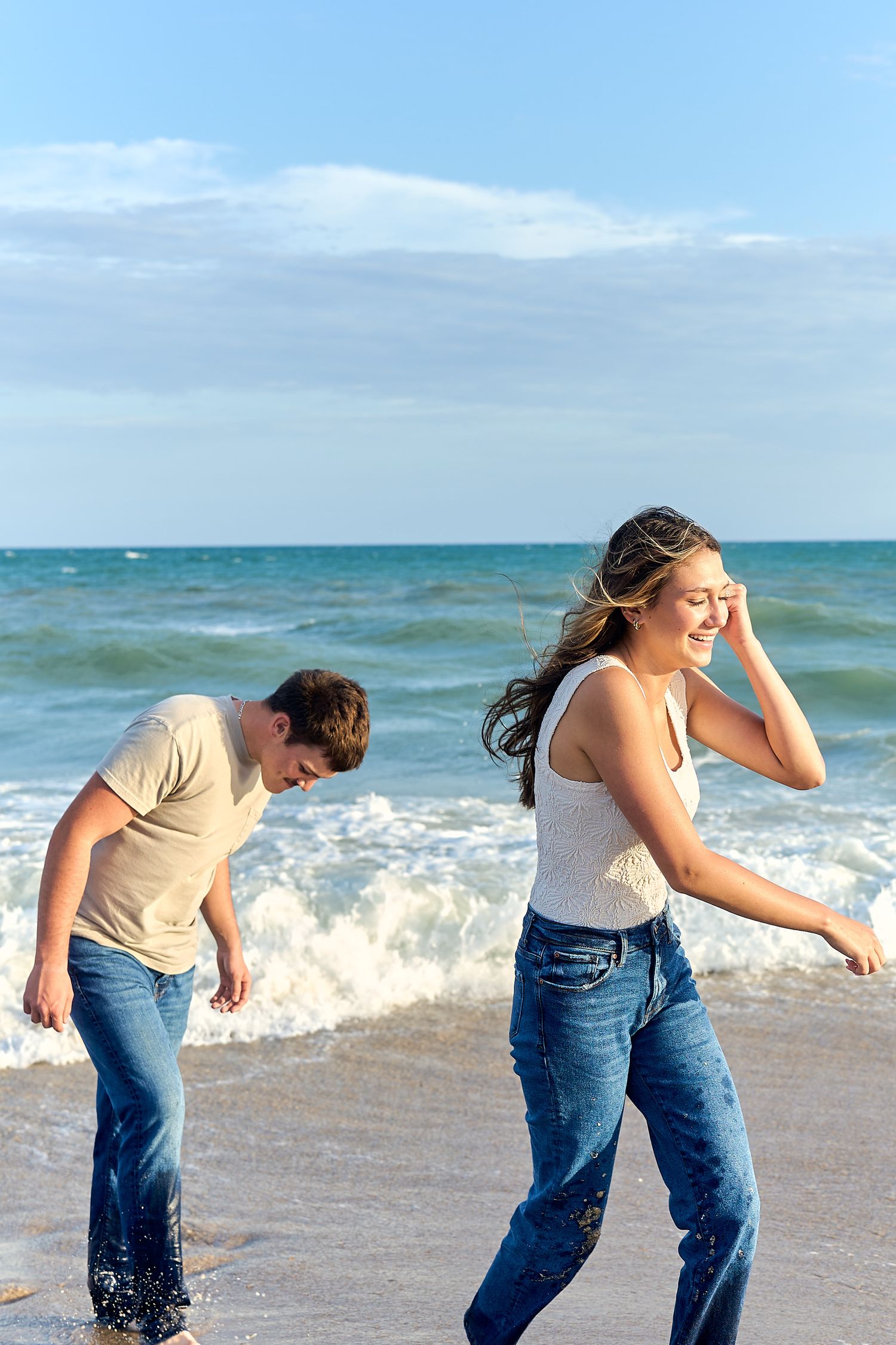 Two people laughing and playing in the ocean waves at the beach on a sunny summer day.
