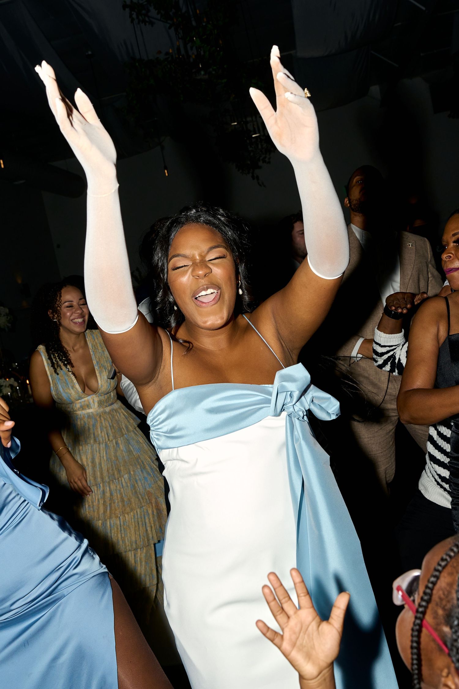Bridesmaid in light blue strapless gown dances joyfully with arms raised at a wedding reception.